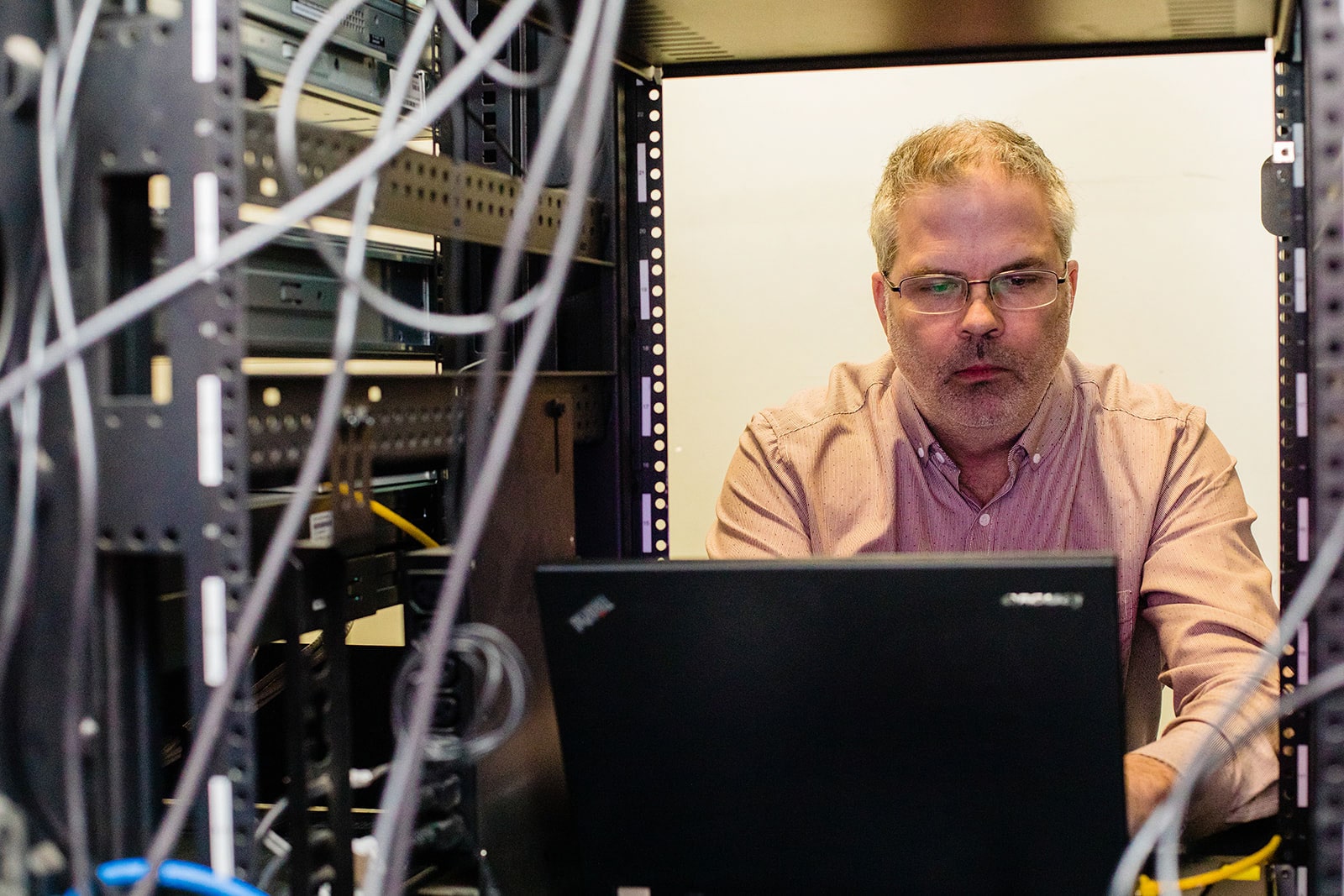 A man works on a laptop inside a computer server system.